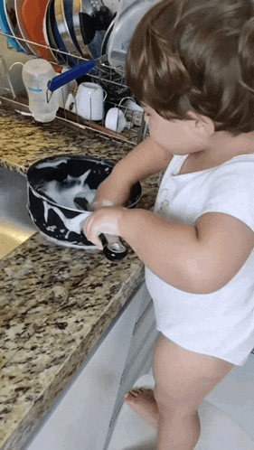 a little boy washing dishes in a kitchen sink