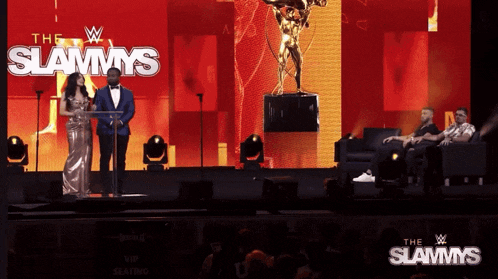 a man and a woman stand on a stage in front of a large screen that says the slammys