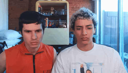 a man in an orange vest and a man in a white t-shirt are looking at each other