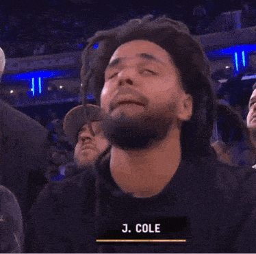 a man with dreadlocks is wearing a black shirt with the name j. cole on it