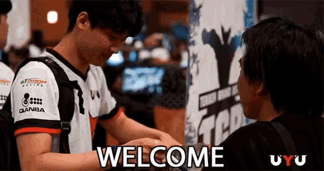 a man shakes another man 's hand in front of a welcome sign