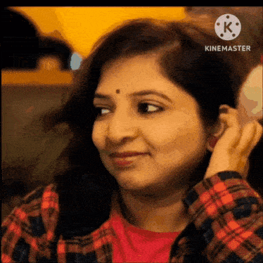 a woman wearing a plaid shirt is smiling and adjusting her ear buds .