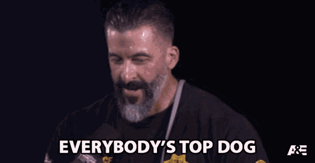 a man with a beard says everybody 's top dog in front of a microphone
