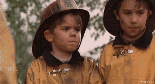 a boy wearing a fireman 's helmet is standing next to another boy wearing a fireman 's jacket