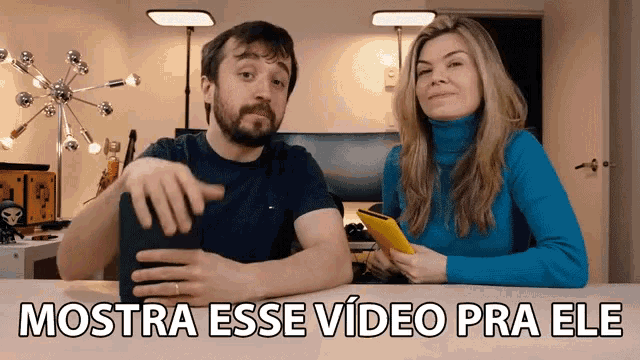 a man and a woman sitting at a table with the words mostra esse video pra ele
