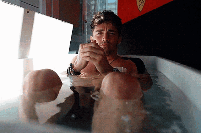 a shirtless man is sitting in a bathtub with a ferrari sign on the wall behind him