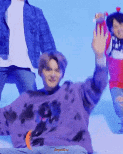 a man in a purple sweater is waving his hand in front of a blue background .