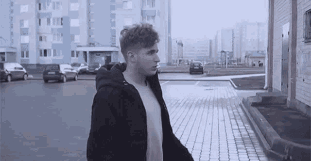 a young man in a black jacket is walking down a brick sidewalk in front of a building .
