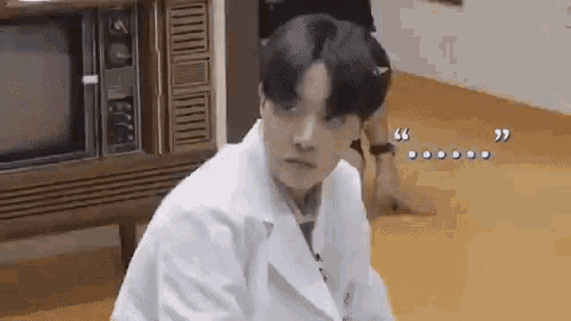a man in a lab coat is sitting on the floor in front of a television .
