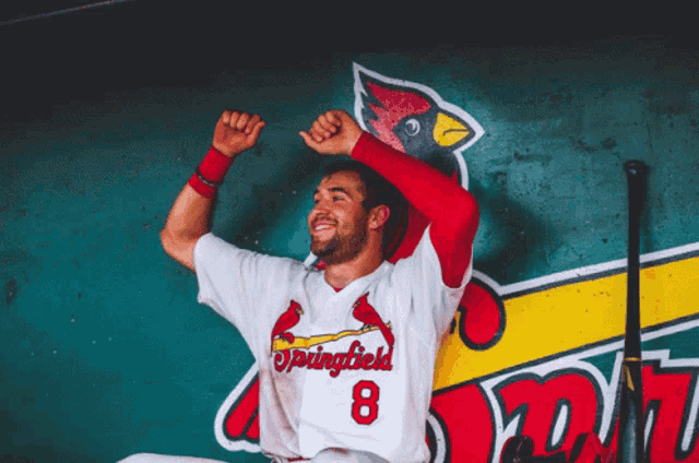 a baseball player for the springfield cardinals is sitting in a dugout with his arms in the air