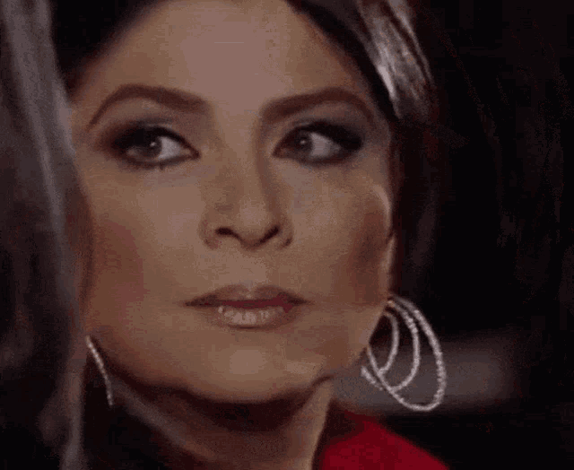 a woman wearing hoop earrings and a red jacket is looking at the camera .
