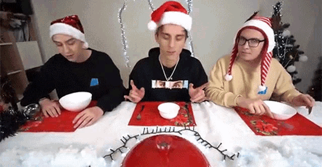 three men wearing santa hats are sitting at a table eating bowls of food .