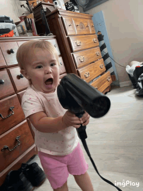 a little girl is holding a hair dryer in her hand