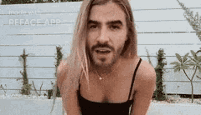 a man with long blonde hair and a beard is wearing a black tank top and a necklace .