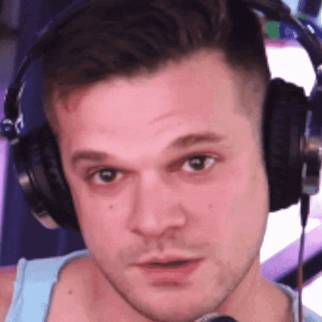 a man wearing headphones and a blue tank top looks at the camera
