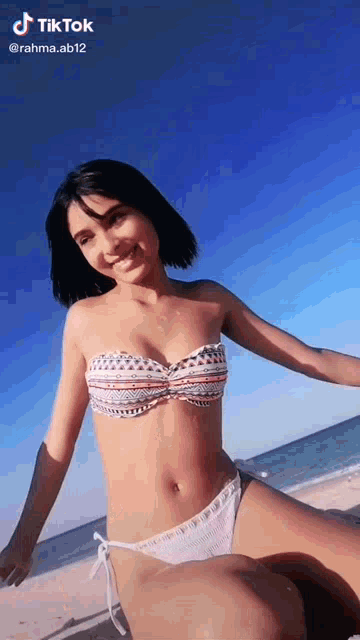 a woman in a bikini is sitting on the beach and smiling at the camera .