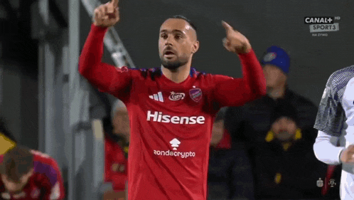 a soccer player wearing a red hisense jersey points upwards