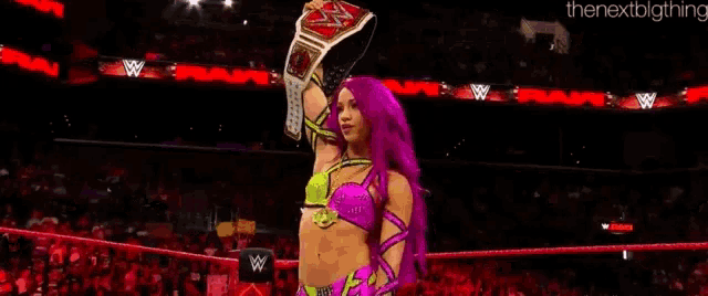 a woman with pink hair is holding a championship belt in a ring .