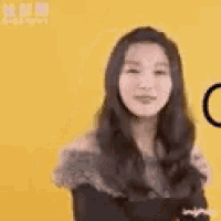 a woman in a black dress is standing in front of a yellow background and smiling .