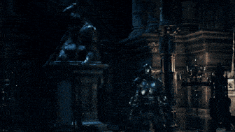 a man in armor stands in a dark room with a statue in the background