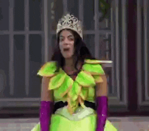 a woman in a green dress and purple gloves is wearing a tiara and making a funny face .