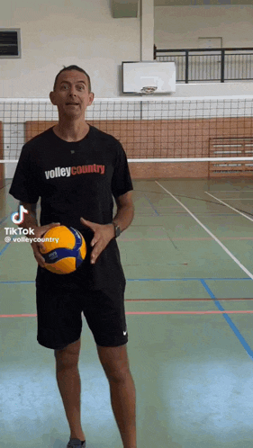 a man in a volley country shirt holds a volleyball in a gym