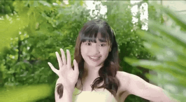 a young woman in a yellow dress is waving her hand in front of a green forest .