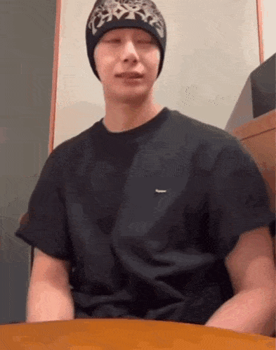 a man wearing a black t-shirt and a beanie is sitting at a table .