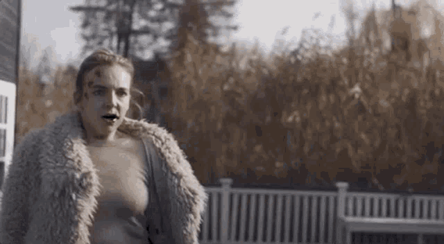 a woman wearing a fur coat is standing in front of a house .