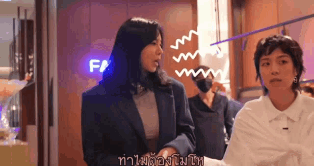 a woman in a blue jacket stands next to another woman in a white shirt in front of a sign that says f /