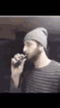 a man with a beard is smoking an electronic cigarette while wearing a beanie .