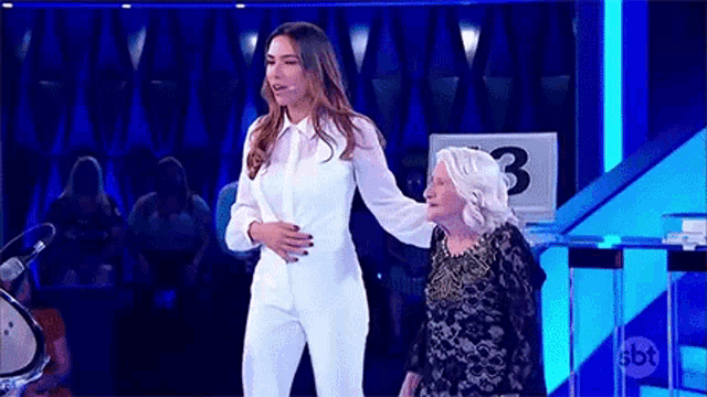 a woman in a white suit is standing next to a woman in a black dress on a stage .