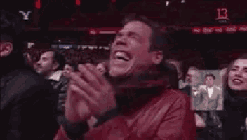 a man in a red jacket is laughing while sitting in a crowd .