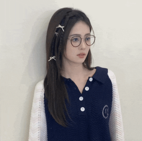 a woman wearing glasses and a vest has a smiley face on her chest