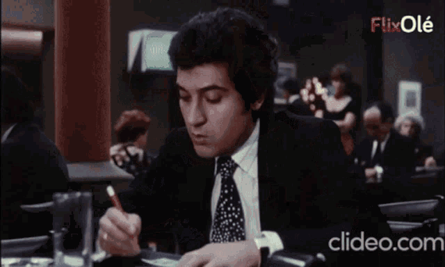 a man in a suit sits at a table with a glass of beer in front of a screen that says flixole on it