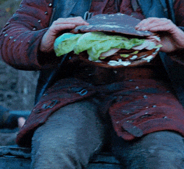 a person in a red jacket is holding a sandwich with lettuce