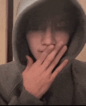 a young man wearing a hoodie is covering his mouth with his hand .