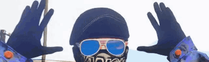 a person wearing a helmet , sunglasses , a mask and gloves is making a peace sign .