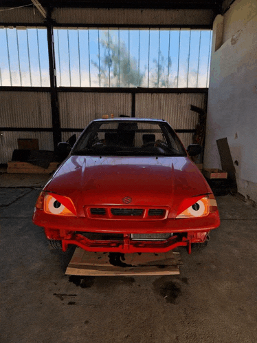 a red suzuki car is parked in a shed