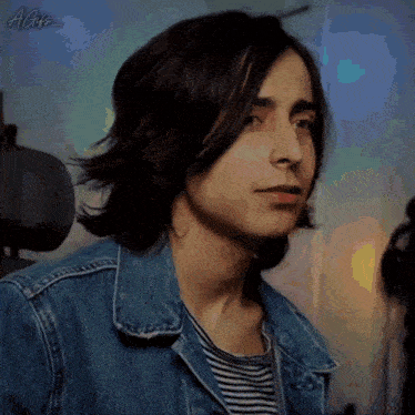 a man with long hair is wearing a denim jacket and striped shirt .