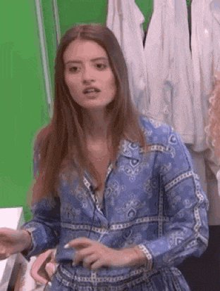 a woman in a blue dress is standing in front of a green screen and making a funny face .