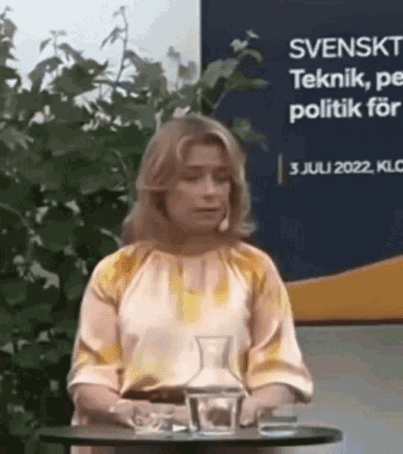 a woman is sitting at a table with a microphone in front of a sign that says svenska teknik , politik for .