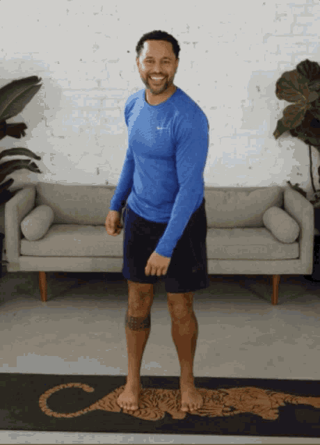 a man in a blue shirt and shorts stands on a yoga mat with the letter c on it