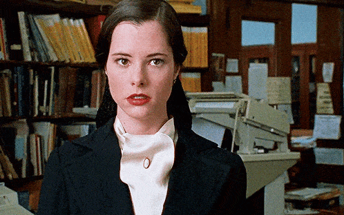 a woman in a black jacket and white shirt stands in front of a printer
