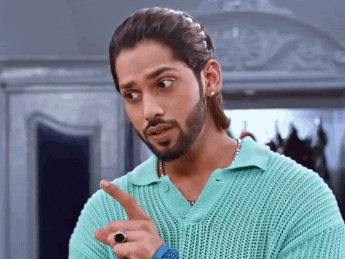 a man with a beard wearing a green sweater and a ring on his finger is pointing .