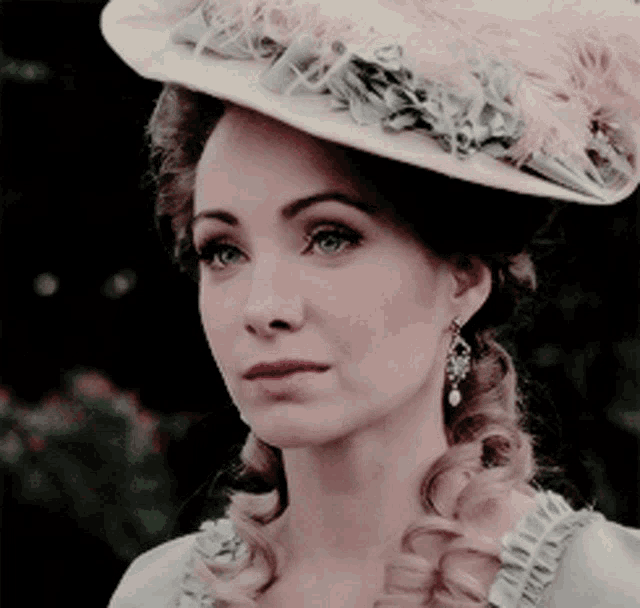 a woman wearing a hat and earrings looks at the camera