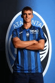 a man in a blue striped shirt is standing with his arms crossed in front of a soccer logo .