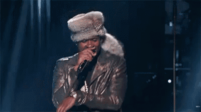 a man in a fur hat and leather jacket is singing into a microphone on a stage .