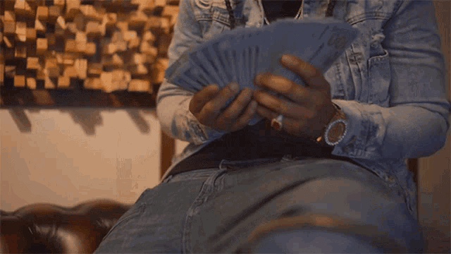 a man in a denim jacket holds a bunch of money in his hands