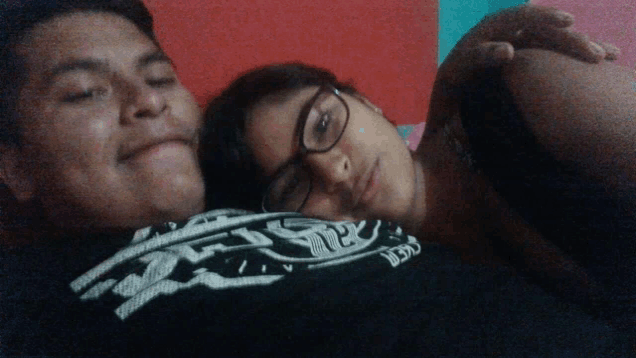 a man and a woman are laying on a bed and the woman is wearing glasses and a shirt that says guess